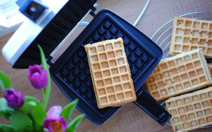 Rozgrzać gofrownicę. Pędzelkiem namoczonym w oleju posmarować całą powierzchnię, na której będą piekły się gofry. Wszystkie składniki wymieszać, w razie potrzeby, gdyby ciasto było za gęste można dodać trochę wody. Porcje ciasta nakładać na rozgrzaną powierzchnię i delikatnie rozprowadzić po całości. Piec zgodnie z instrukcją przez kilka minut. Gotowe gofry studzić na kratce.